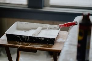 A paint roller and tray with white paint on a wooden table, indicating a renovation work. — Natural hazard zone disclosure re