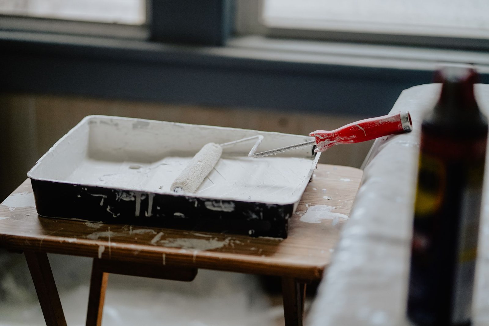 A paint roller and tray with white paint on a wooden table, indicating a renovation work. — Natural hazard zone disclosure re